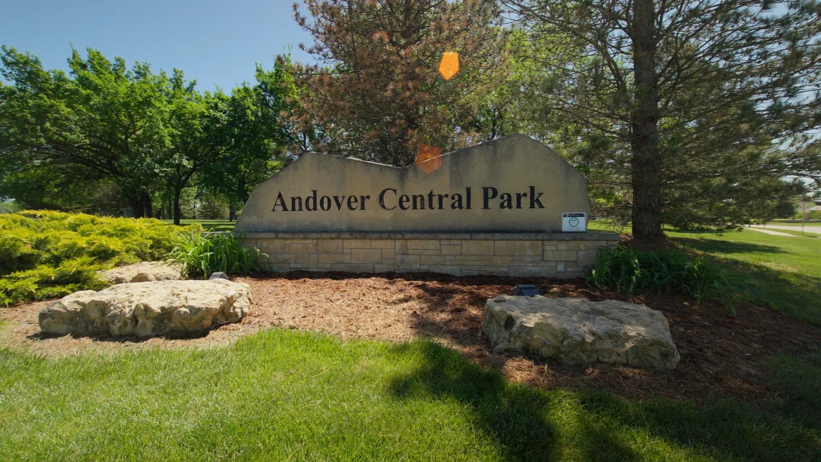 Stone entrance sign for Andover Central Park with trees and green lawn